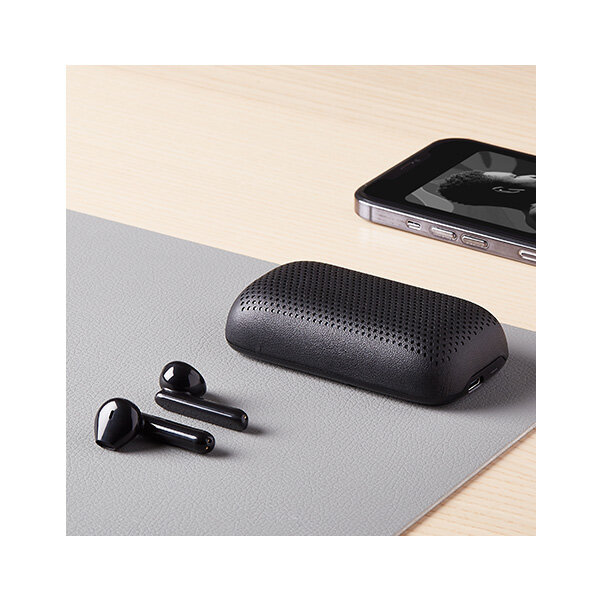Słuchawki bezprzewodowe z głośnikiem Lexon Speakerbuds LA127N czarne leżące na stoliku obok telefonu